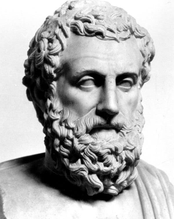 Black and white image of sculpture of Greek Philosopher Aristotle. He has curly short hair, a moustache and beard.