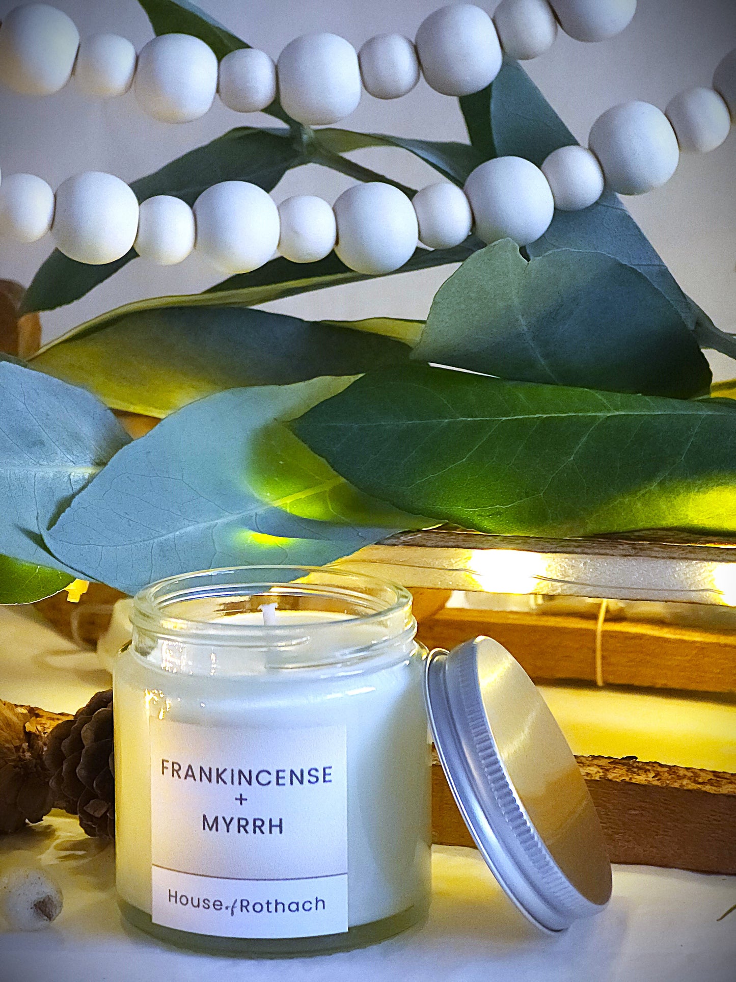 frankincense and myrrh candles in clear jar with silver metal lids with festive decorations in the background.